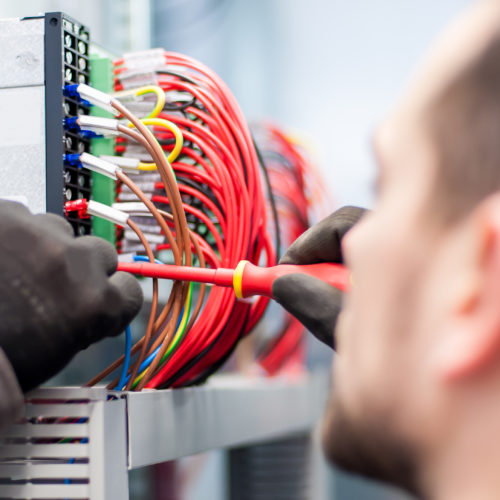 Closeup of electrician engineer works with electric cable wires of fuse switch box. Electrical equipment